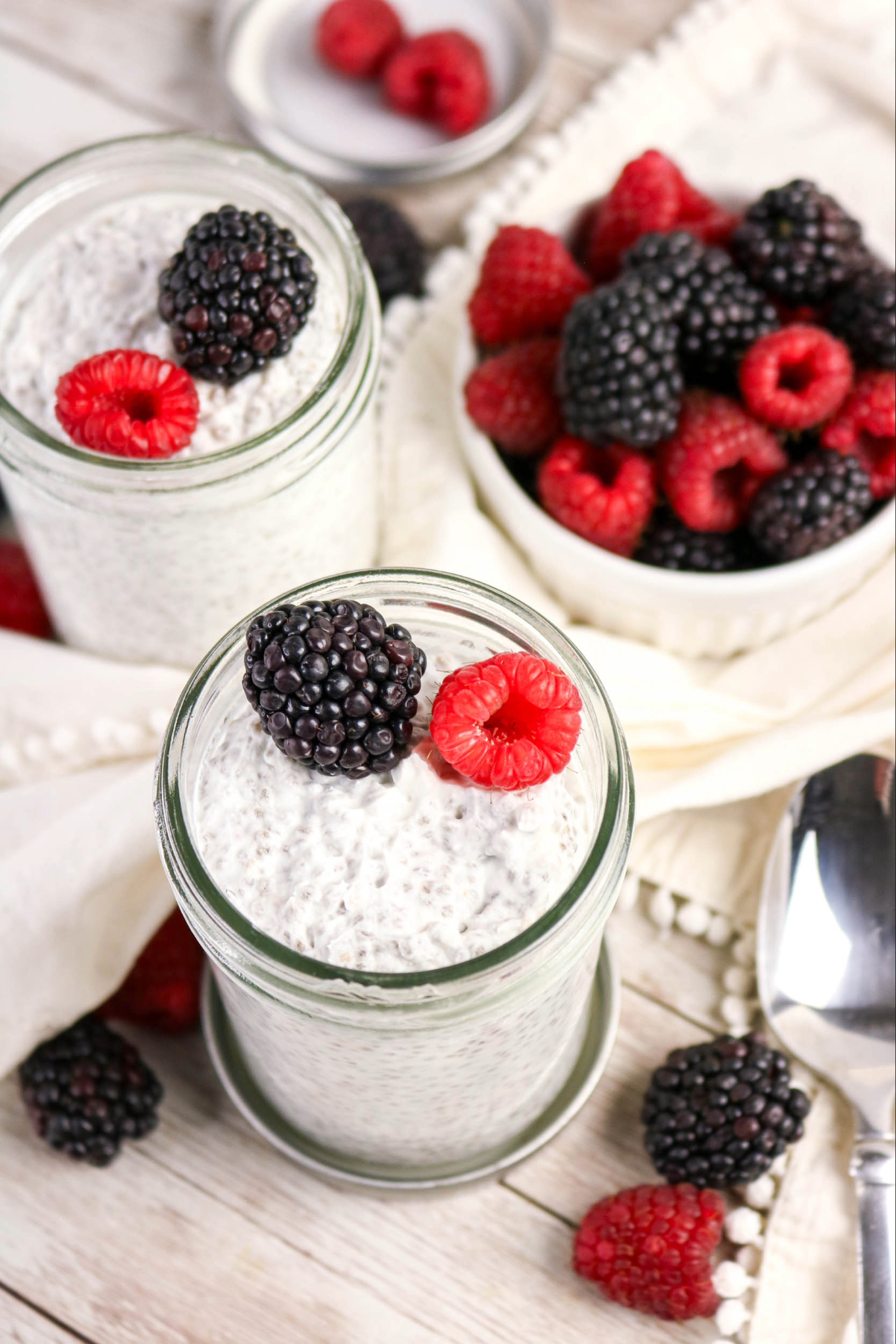Top view of two jars with chia pudding with a small bowl of berries on the side.