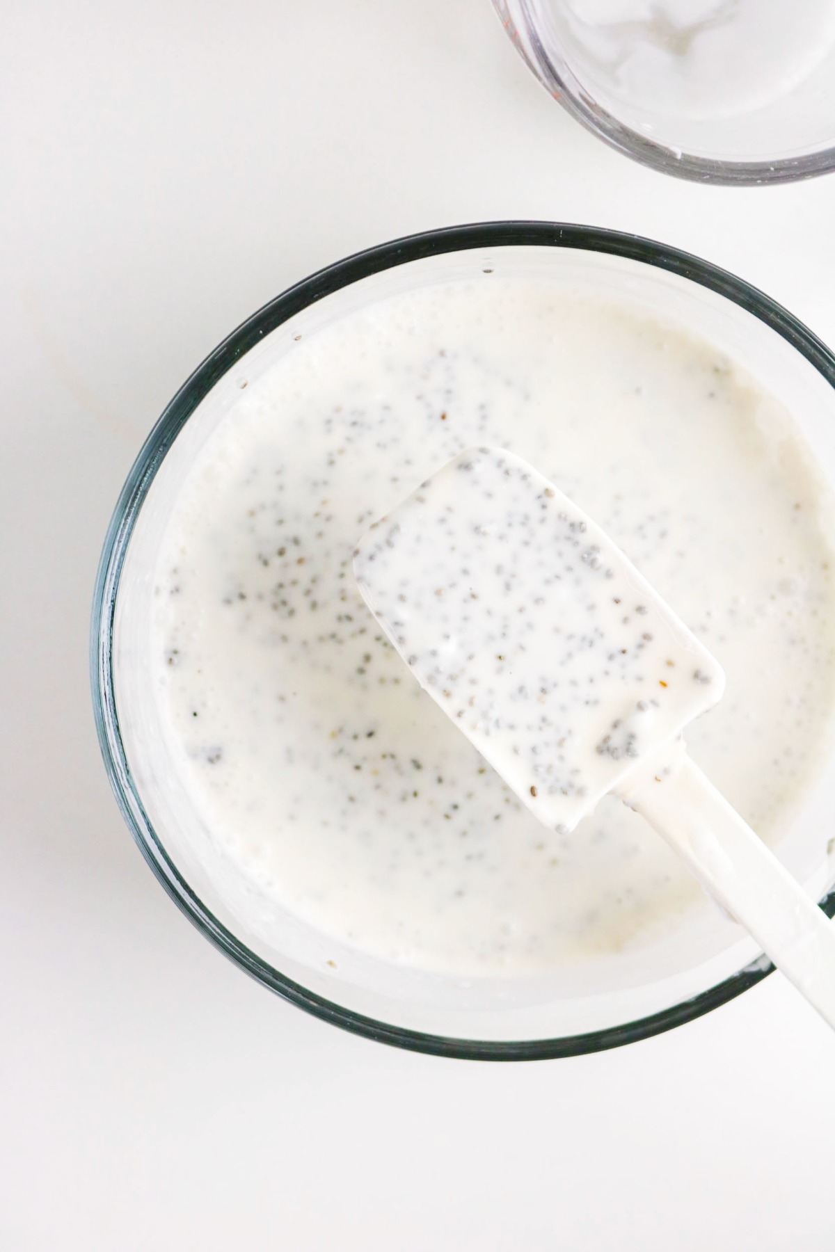 Mixed ingredients for chia pudding in a mixing bowl with rubber spatula.