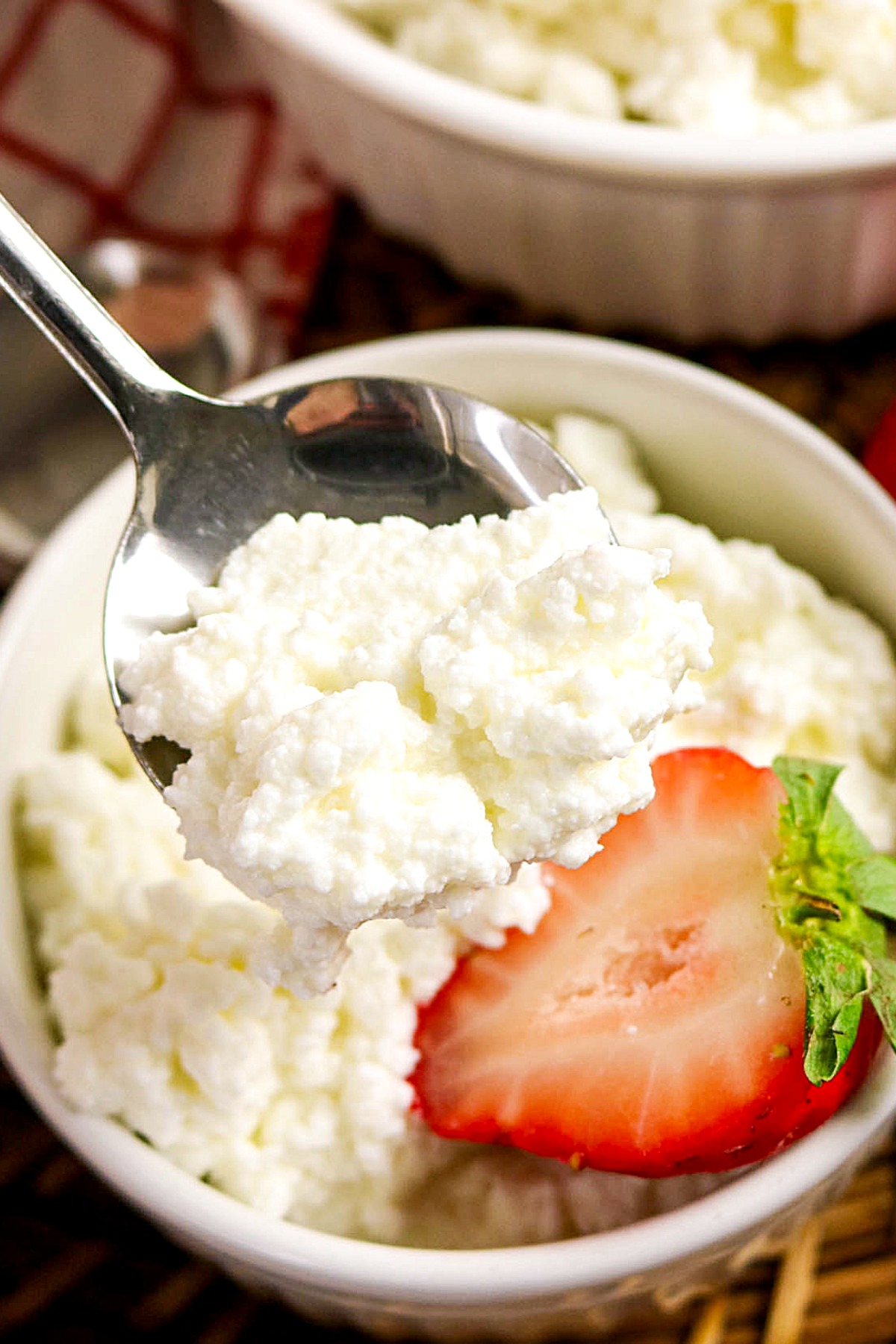 Spoonful of homemade cottage cheese scooping from a white serving bowl.