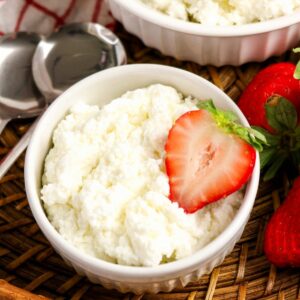homemade cottage cheese in a white bowl with strawberries on the side.