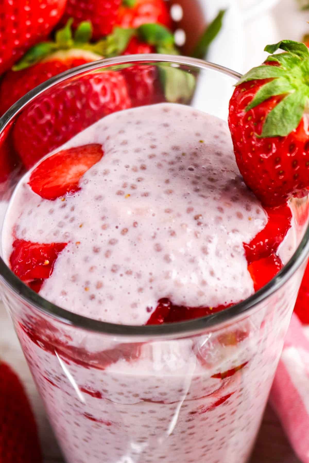 Close view of strawberry chia pudding in a parfait glass with fresh strawberries.