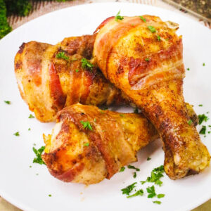 cooked bacon wrapped chicken drumsticks on a white plate.