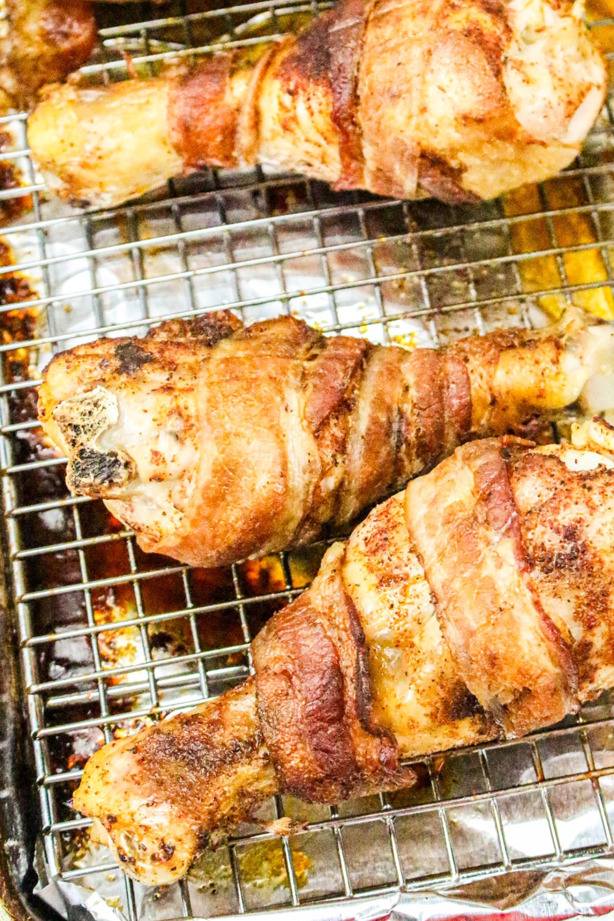 Cooked drumsticks wrapped with bacon on a wire rack over a baking sheet.
