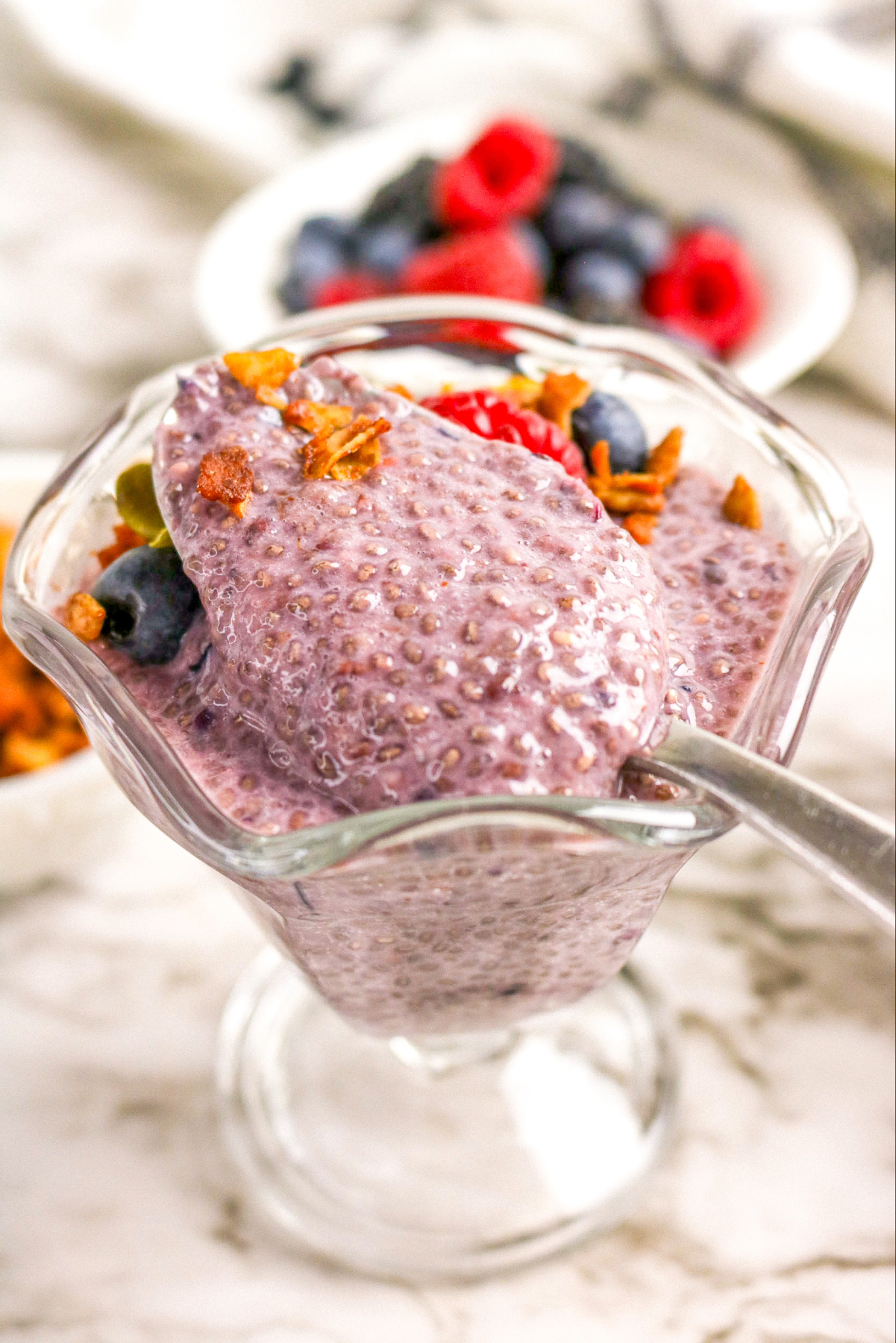 Chia pudding made with a mix of berries in a parfait glass with a spoon ready to scoop out.