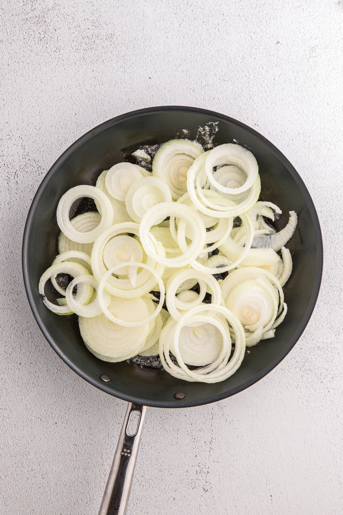 Sliced onions in a skillet before sautéing.