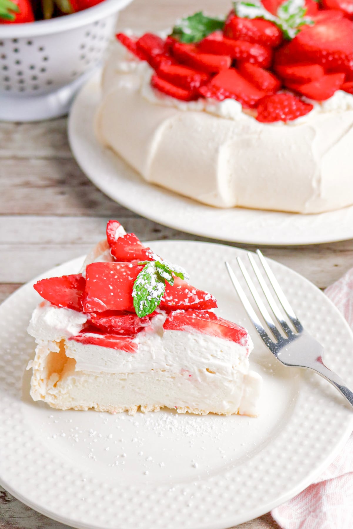 A slice of pavlova on a white plate with the cake in the background.