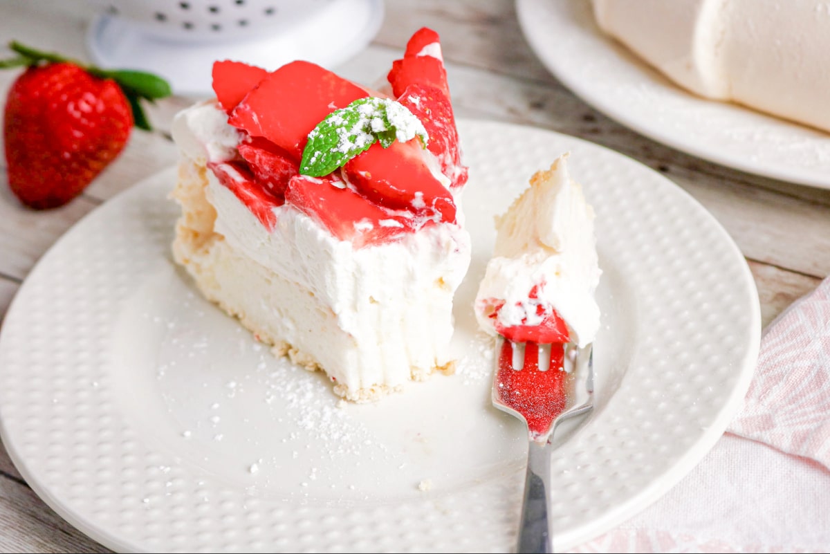 A slice of pavlova cake with a fork topped with cake on the side.