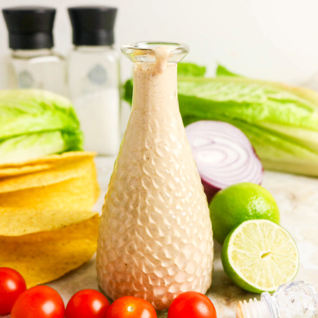 Taco salad dressing in a clear container with fresh tomatoes on the side.