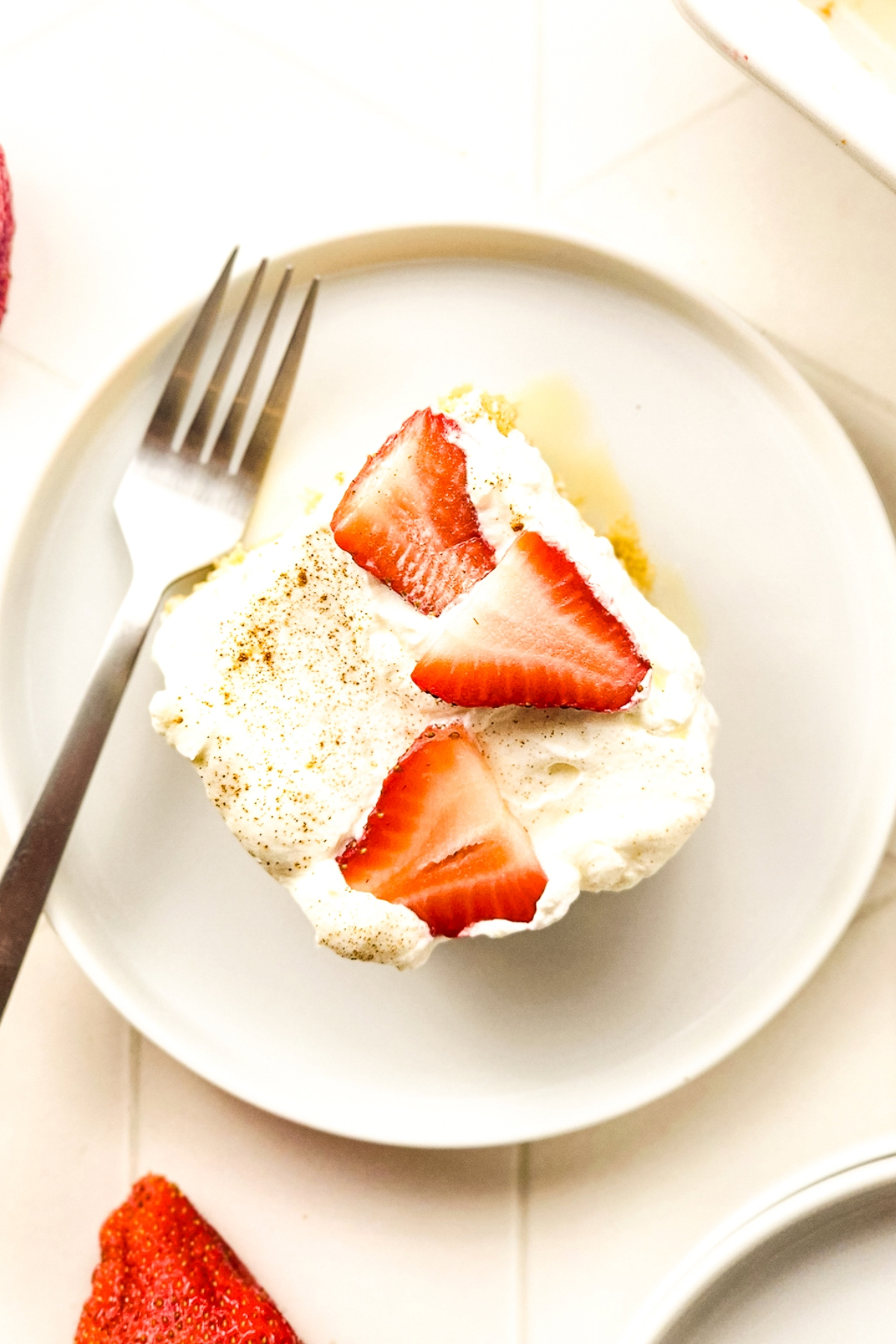 Overhead view of a square slice of tres leches cake on a white plate with a fork on the side.