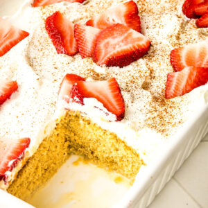Tress Leches cake in a white baking dish with a piece cut out exposing the cake.