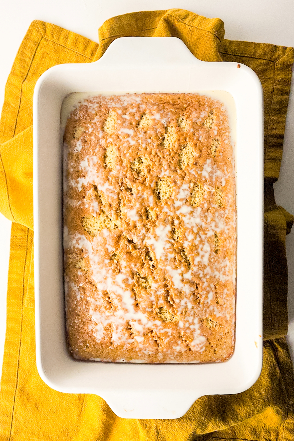Cooked cake poked with holes and milk mixture poured over the cake.