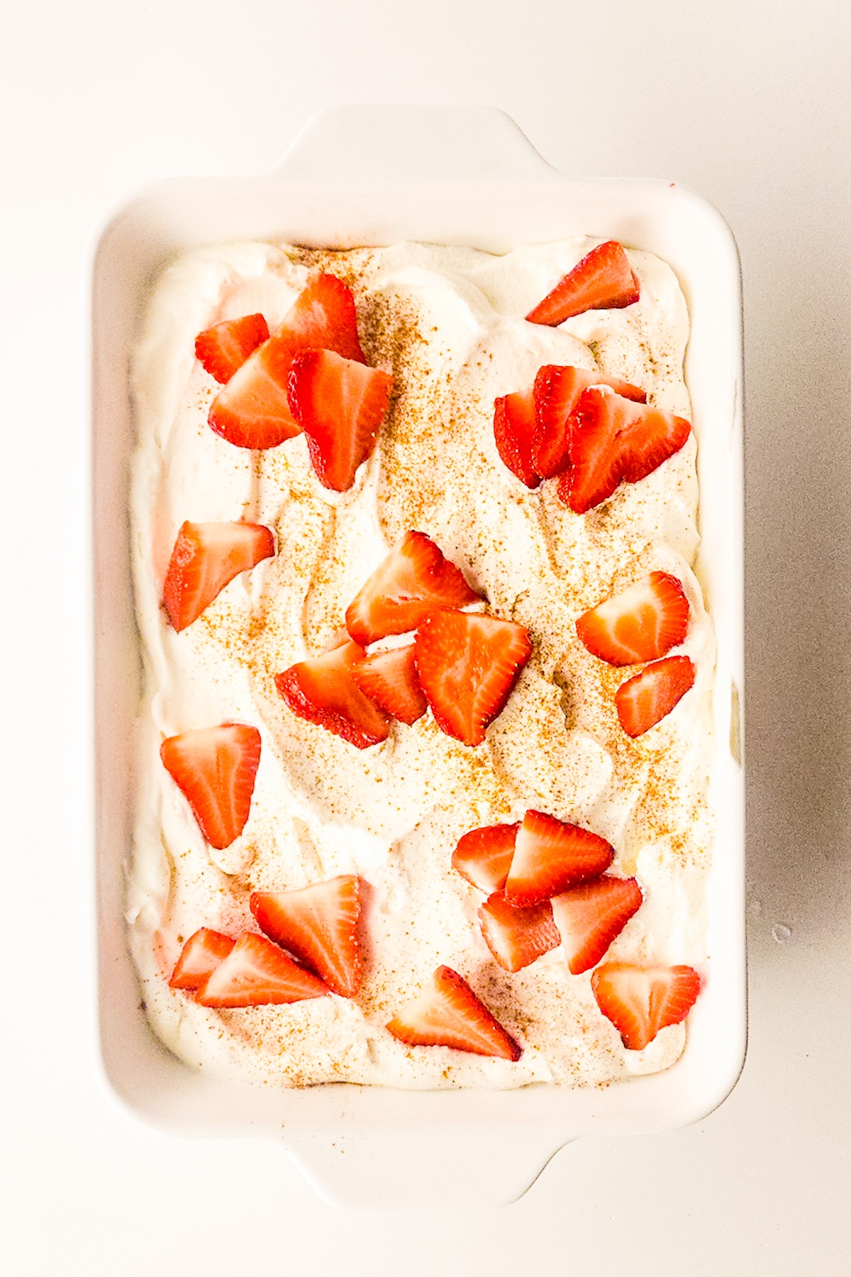 Tres leches cake garnished with sliced strawberries and sprinkles of cinnamon.