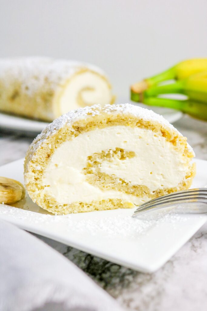 A slice of banana roll cake with cream cheese filling on a white plate.