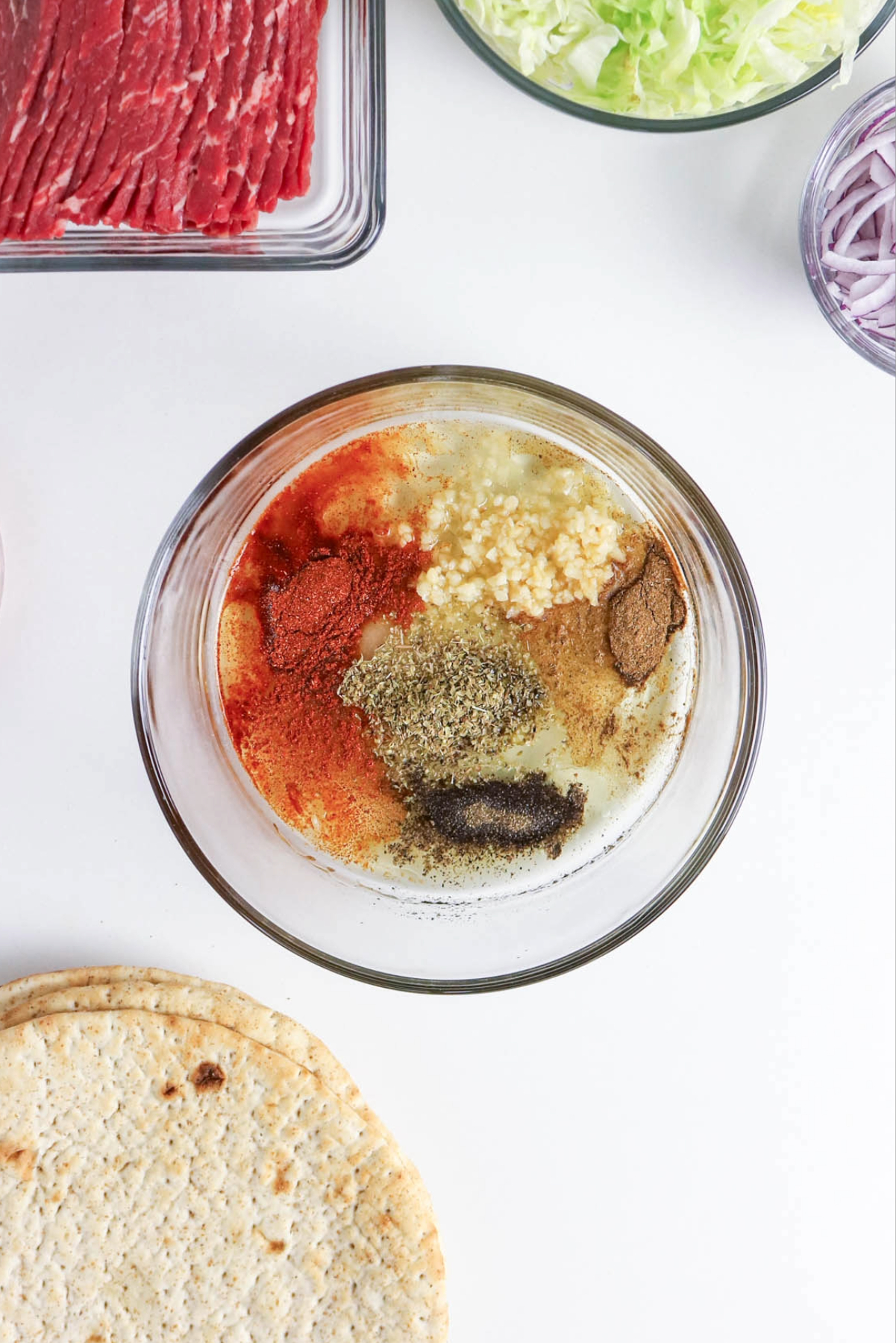 Spices in a clear mixing bowl for beef gyros.
