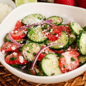 cucumber strawberry salad with feta and sliced onions in a white serving bowl.