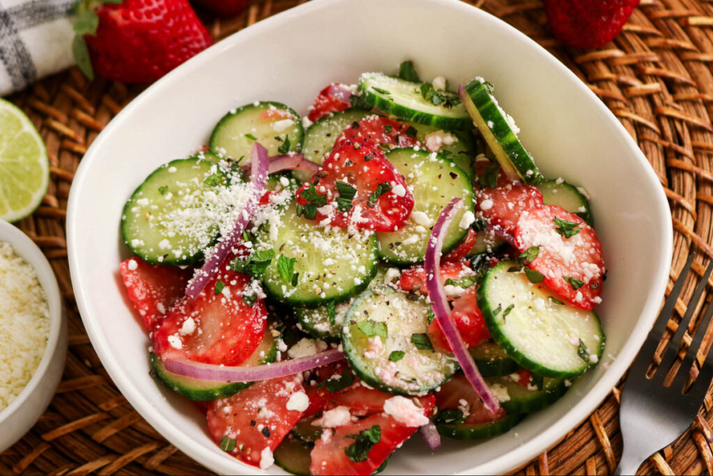 Summer salad in a white serving dish made with sliced strawberries and cucumbers.