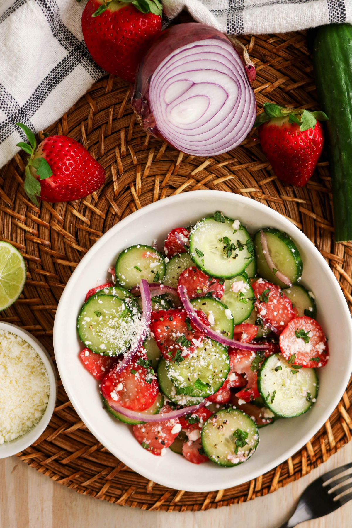 Top view of a table with ingredients surrounding a cucumber strawberry salad.