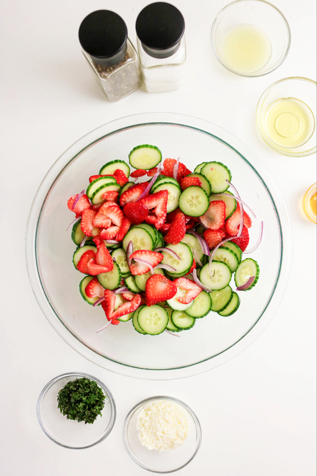 sliced cucumbers and strawberries in a clear large mixing bowl.