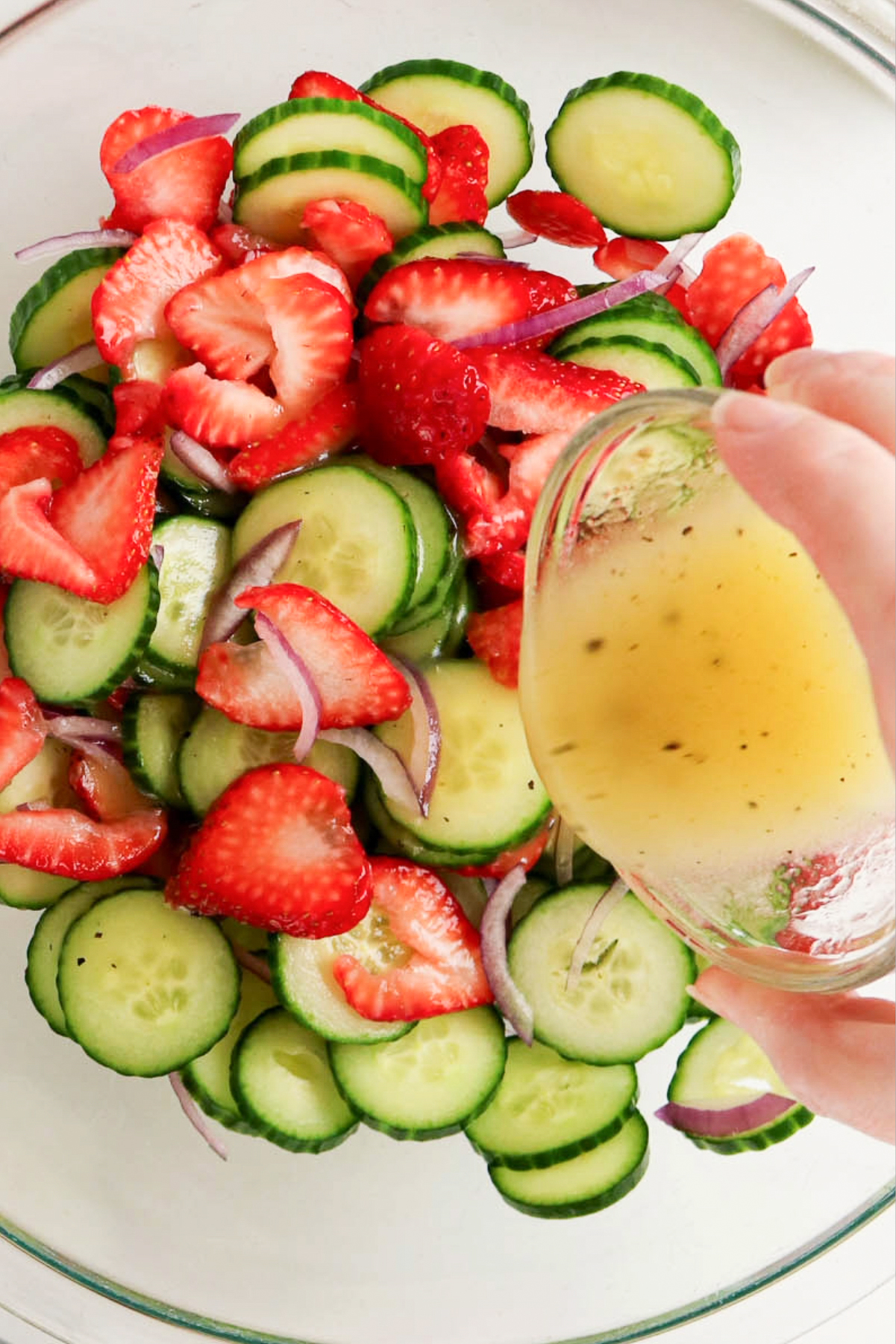 Adding dressing to sliced strawberries and cucumbers.