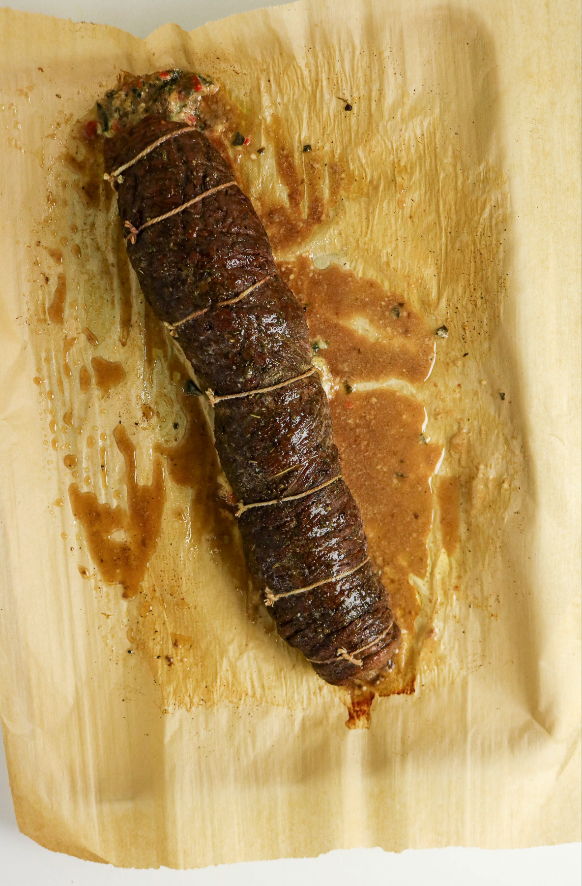 Cooked rolled flank steak on parchment lined cutting board.