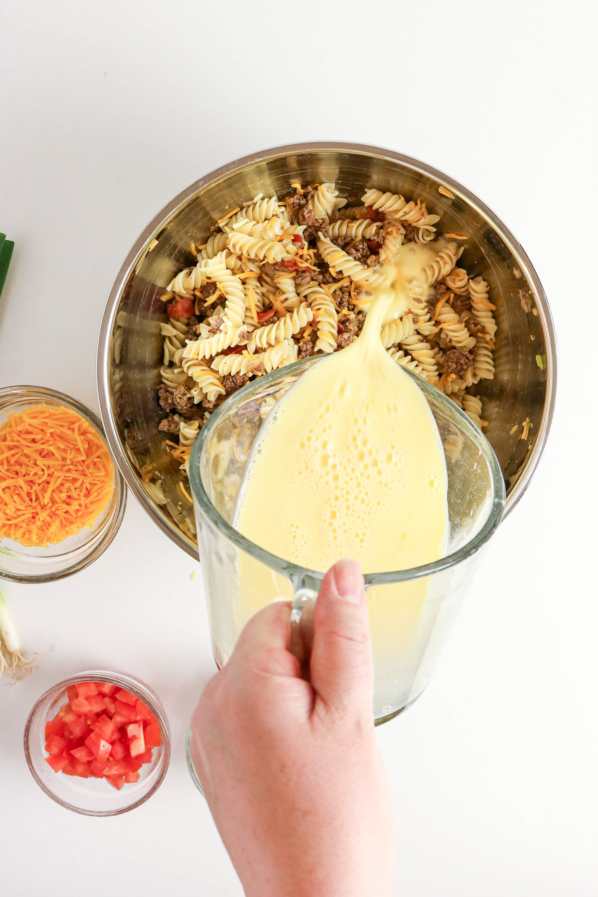 Pouring milk and egg mixture over cheeseburger casserole ingredients.