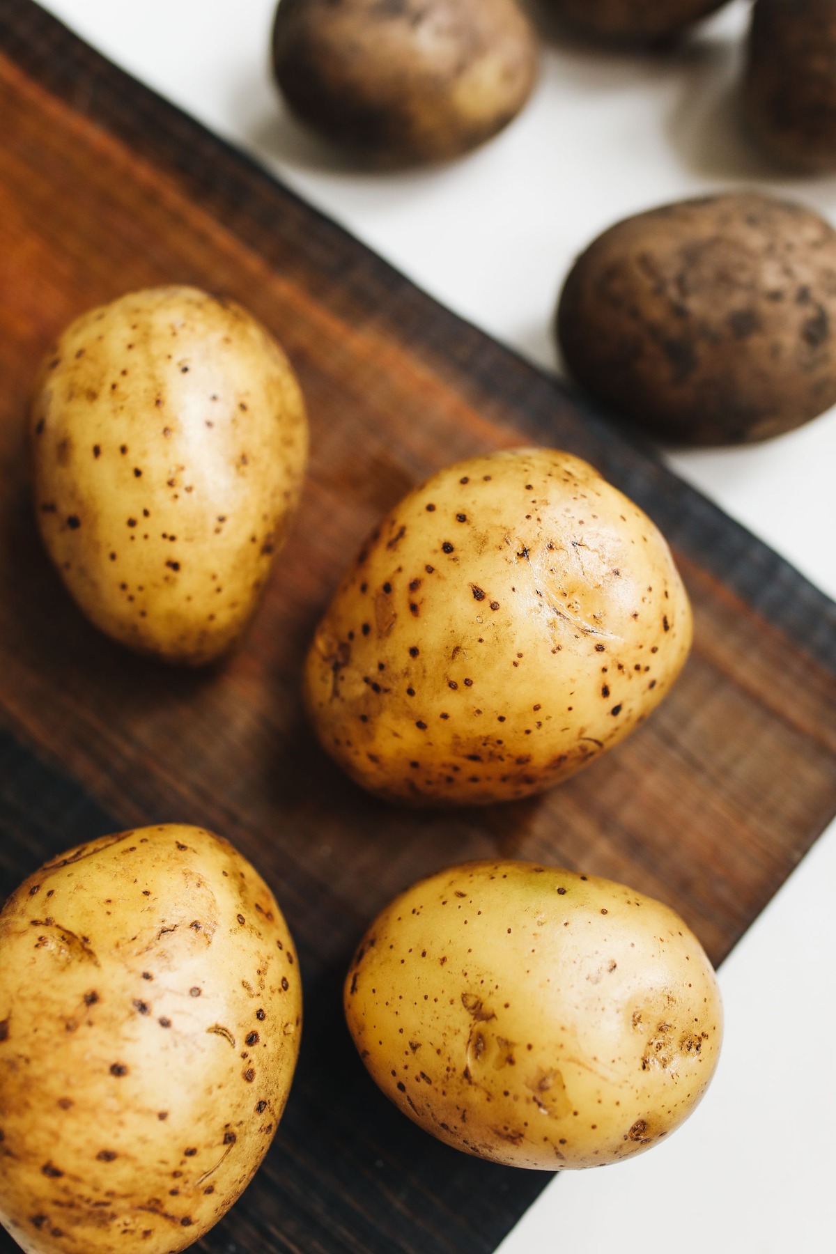 Clean russet potatoes on a wooden cutting board.