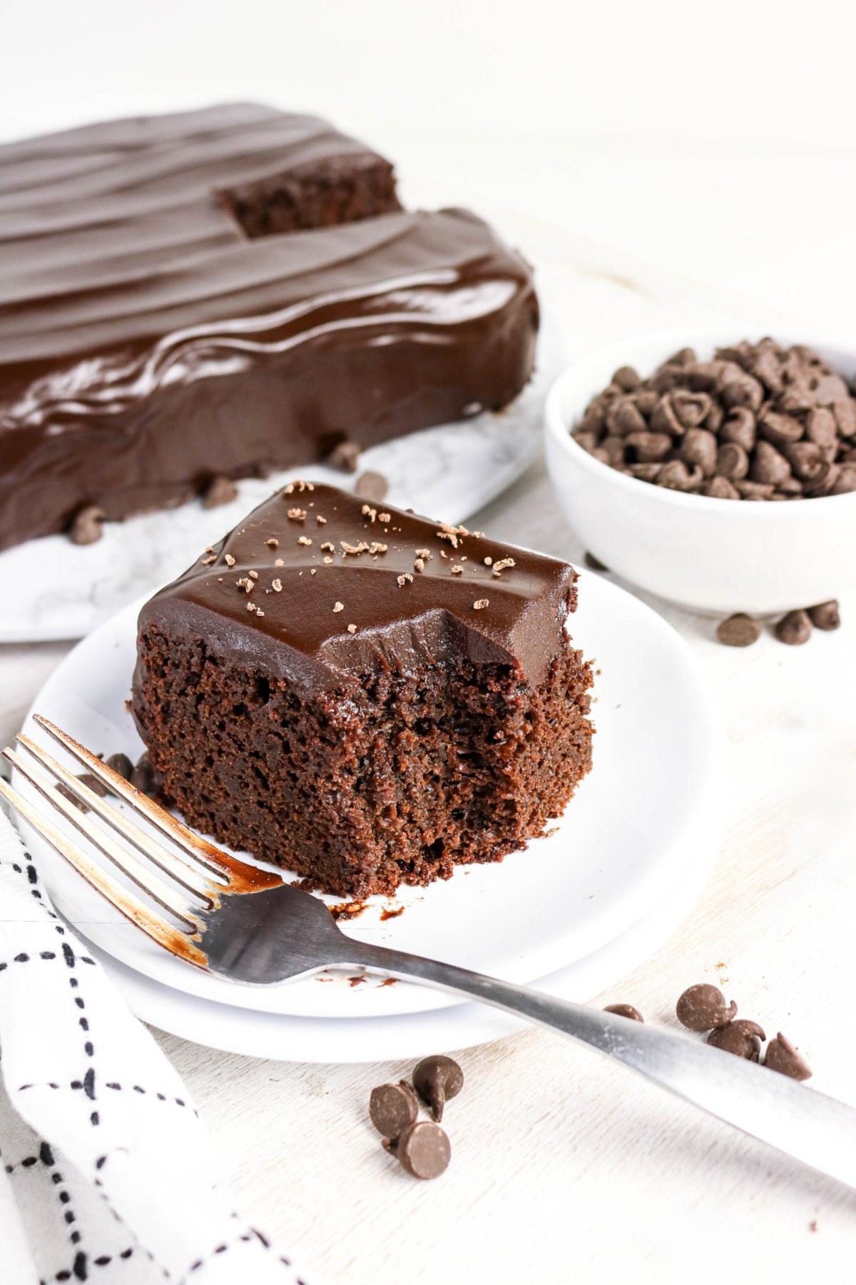 Slice of chocolate cake with the whole cake in the background.