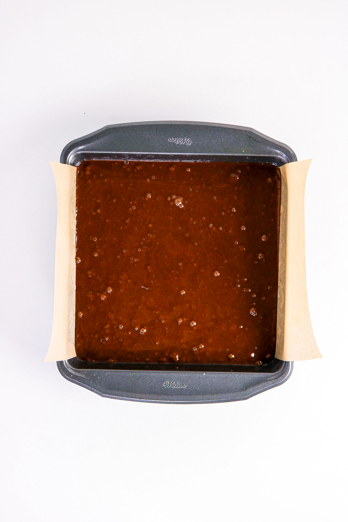Cake batter in a parchment lined square cake pan before baking.