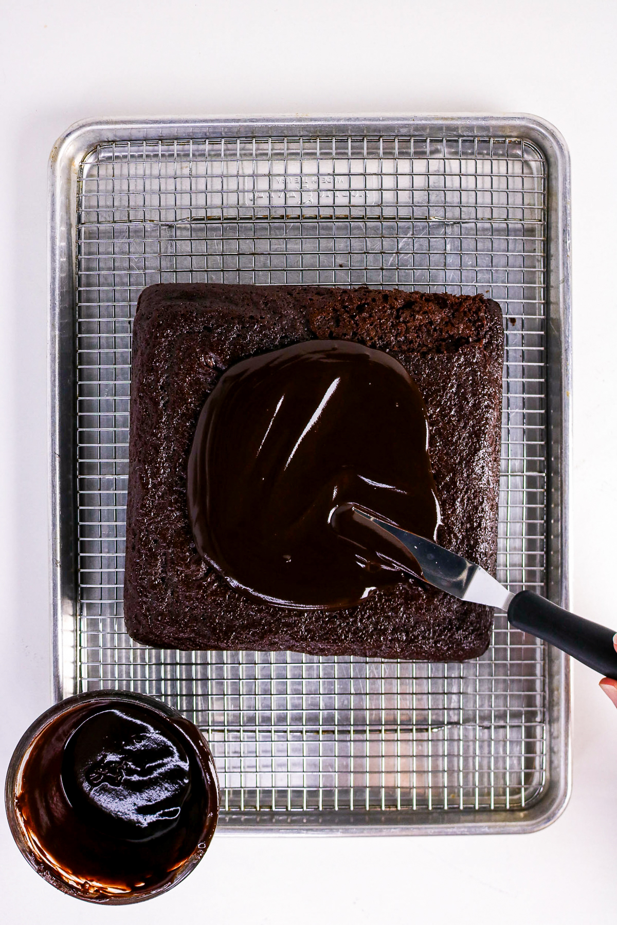 Frosting a chocolate cake on a baking cooling rack.