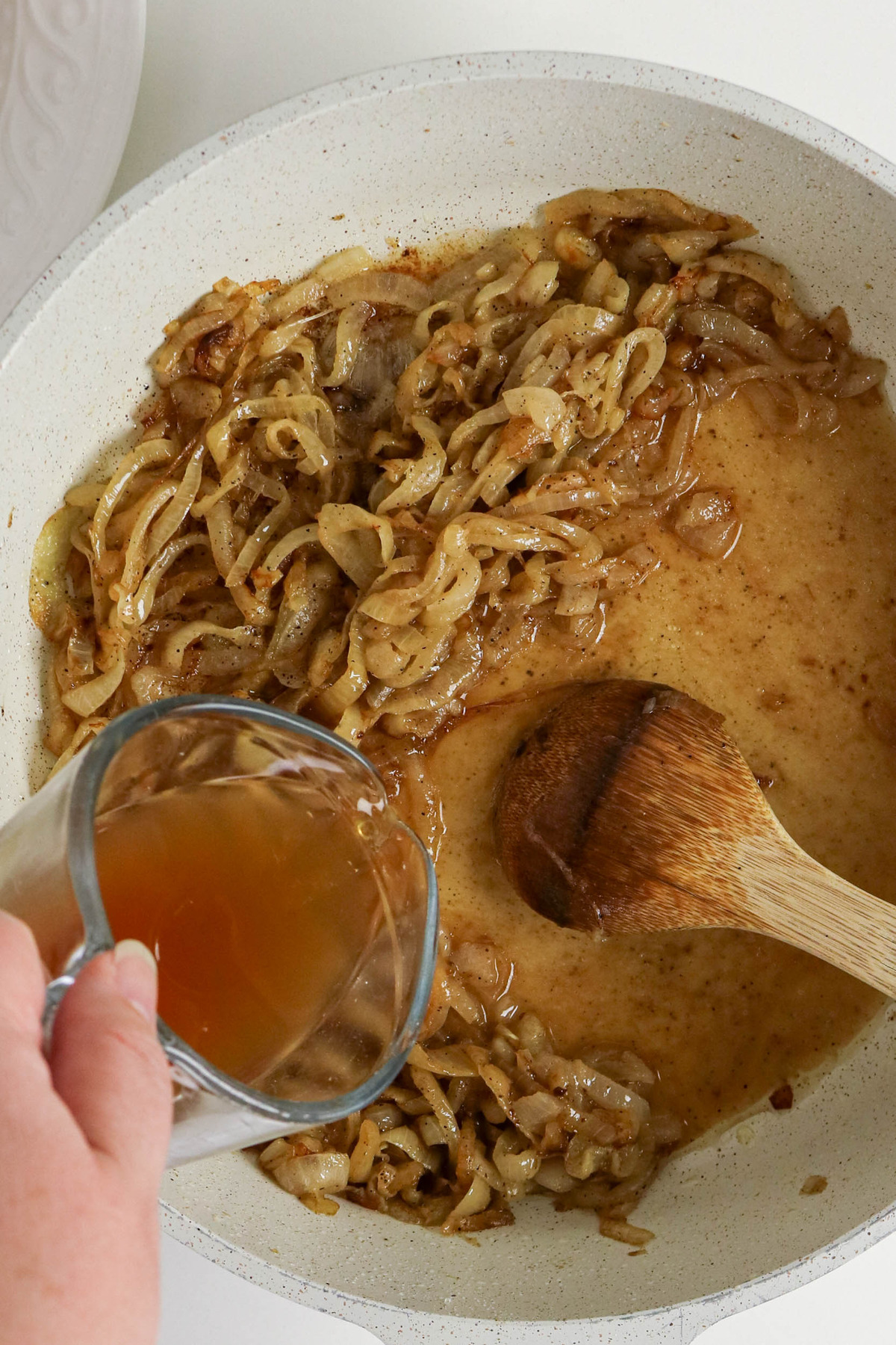 Beef broth added to caramelized onions in a skillet.