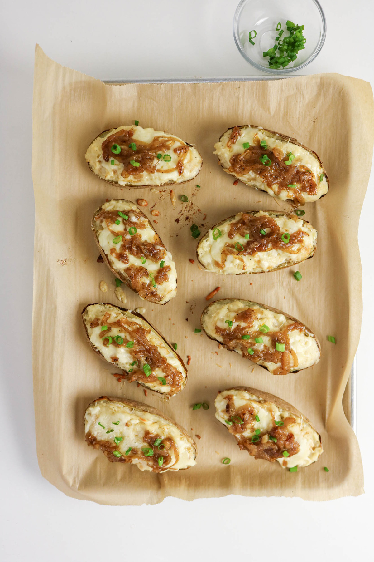 Twice baked potatoes on a baking sheet with French onion and green onions.
