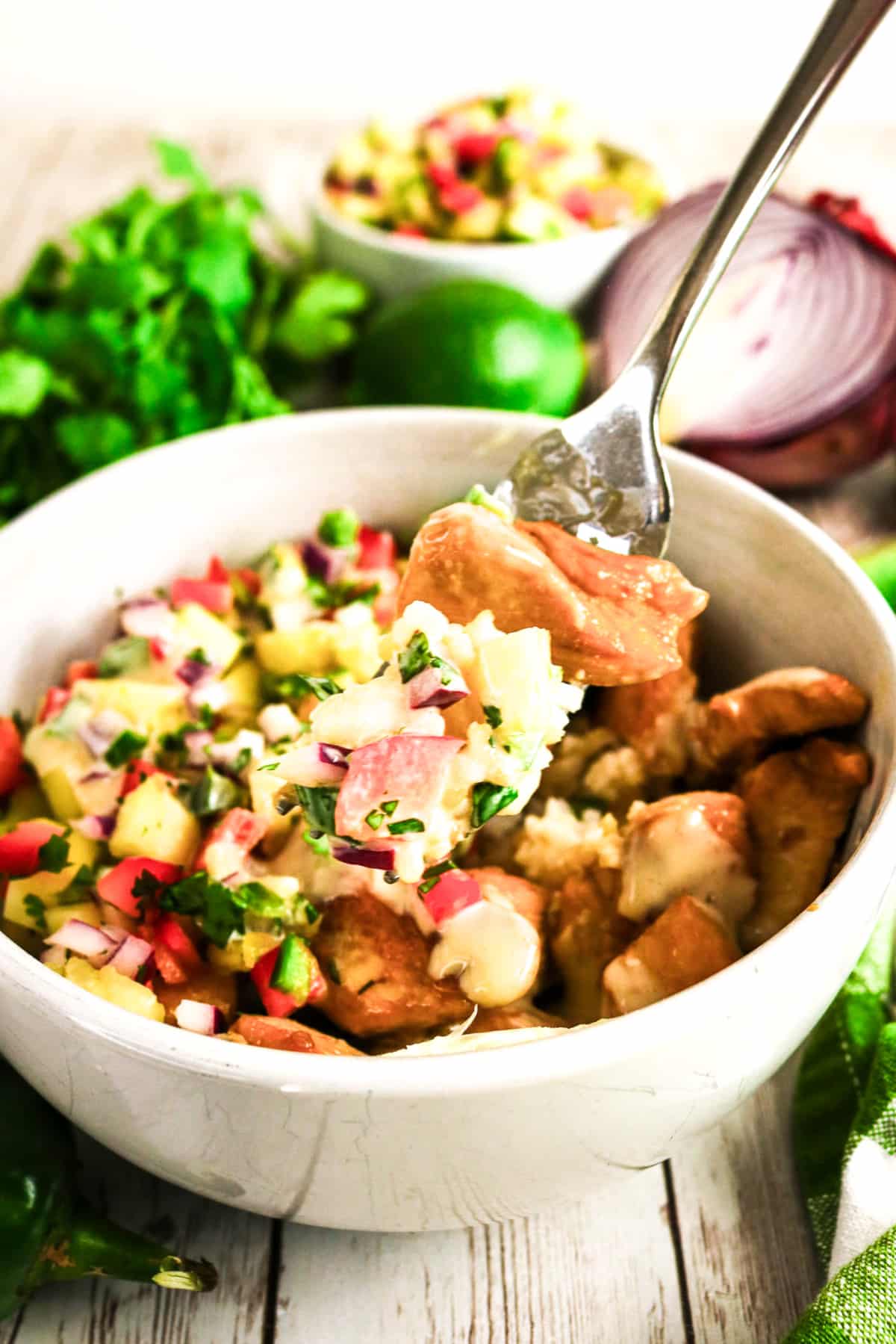 Chicken with pineapple salsa in a white bowl with a fork on the side.