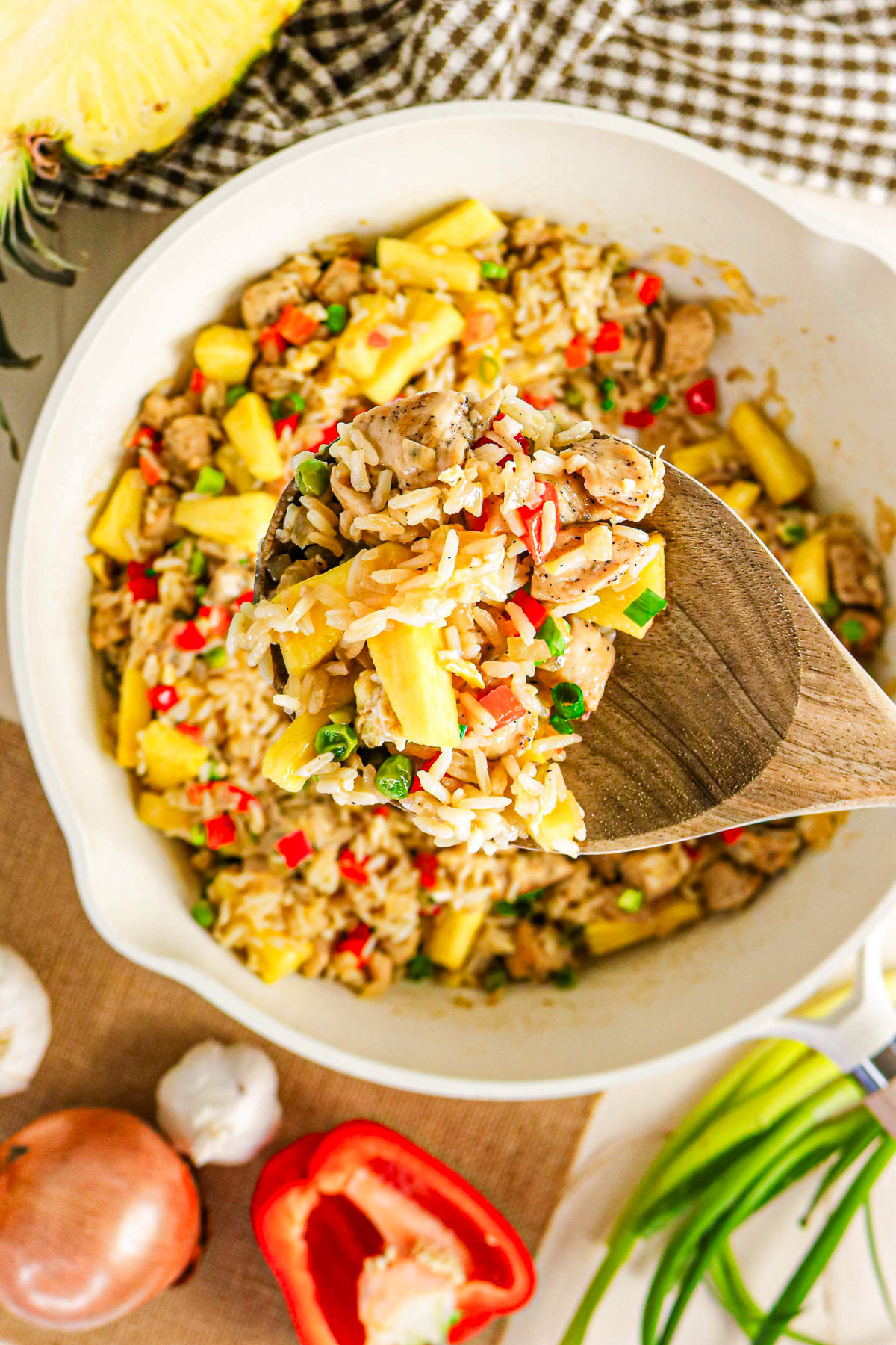 A wooden spoonful of fried rice in a skillet with pineapple and chicken.