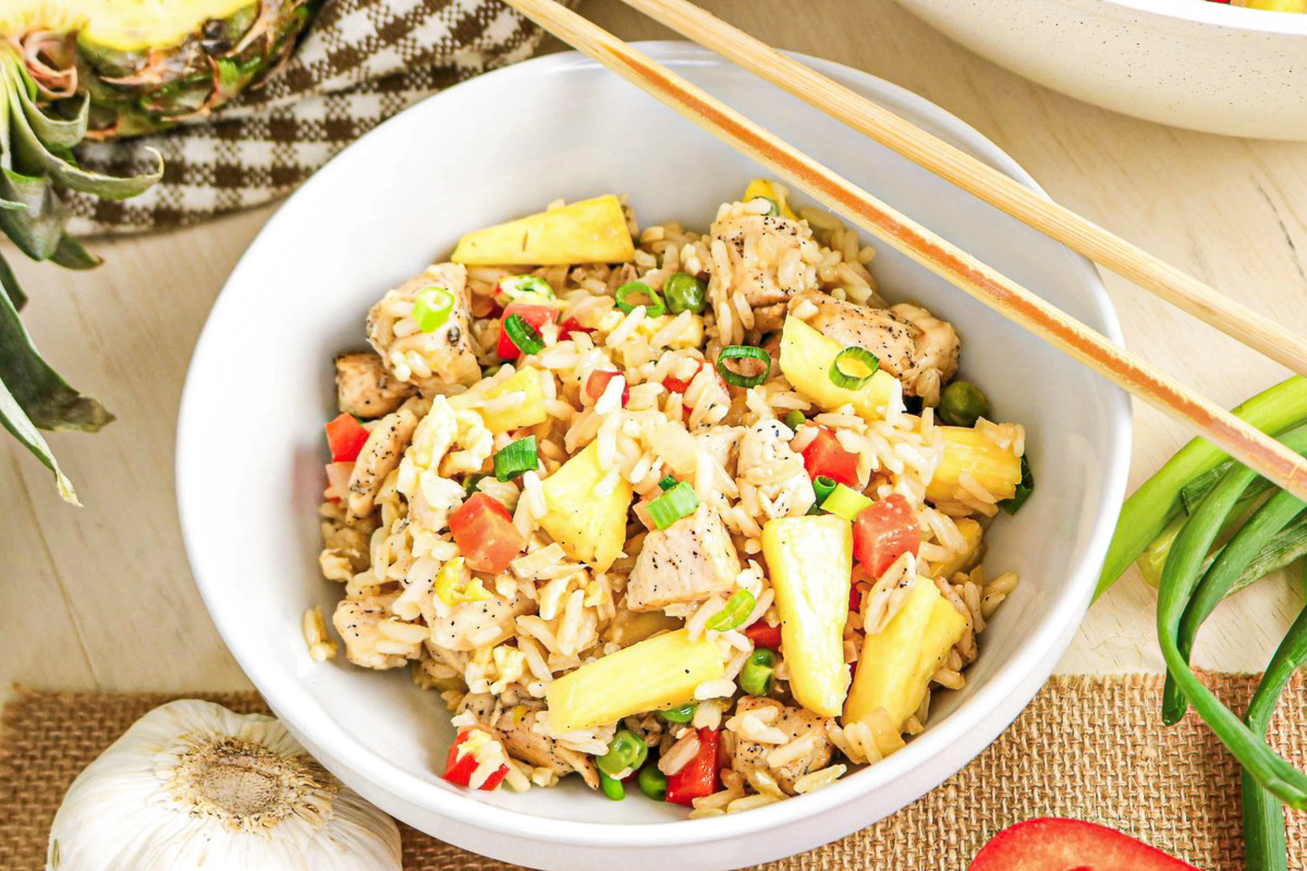 A white bowl filled with fried rice with chopsticks on the side of the bowl.