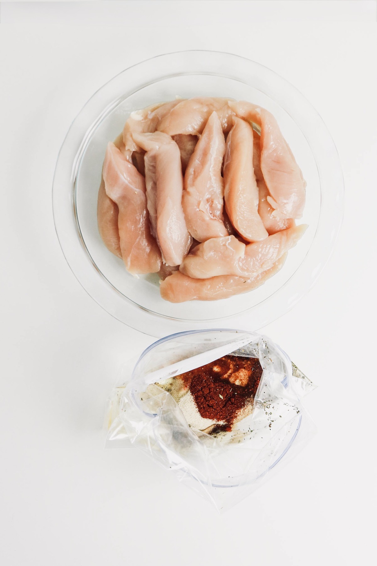 Chicken tenders in a mixing bowl with marinade in a plastic bag on the side.