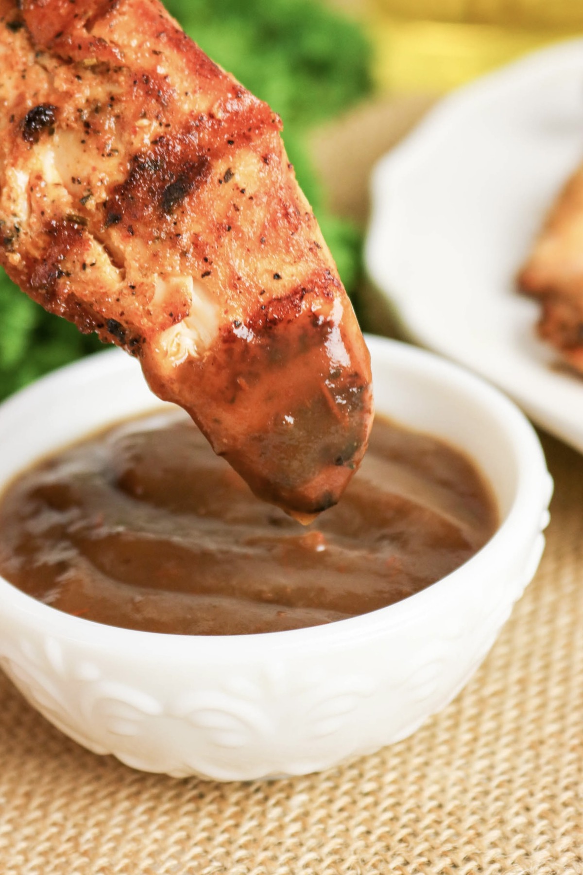 Chicken tender dipped in BBQ sauce from a small white bowl.