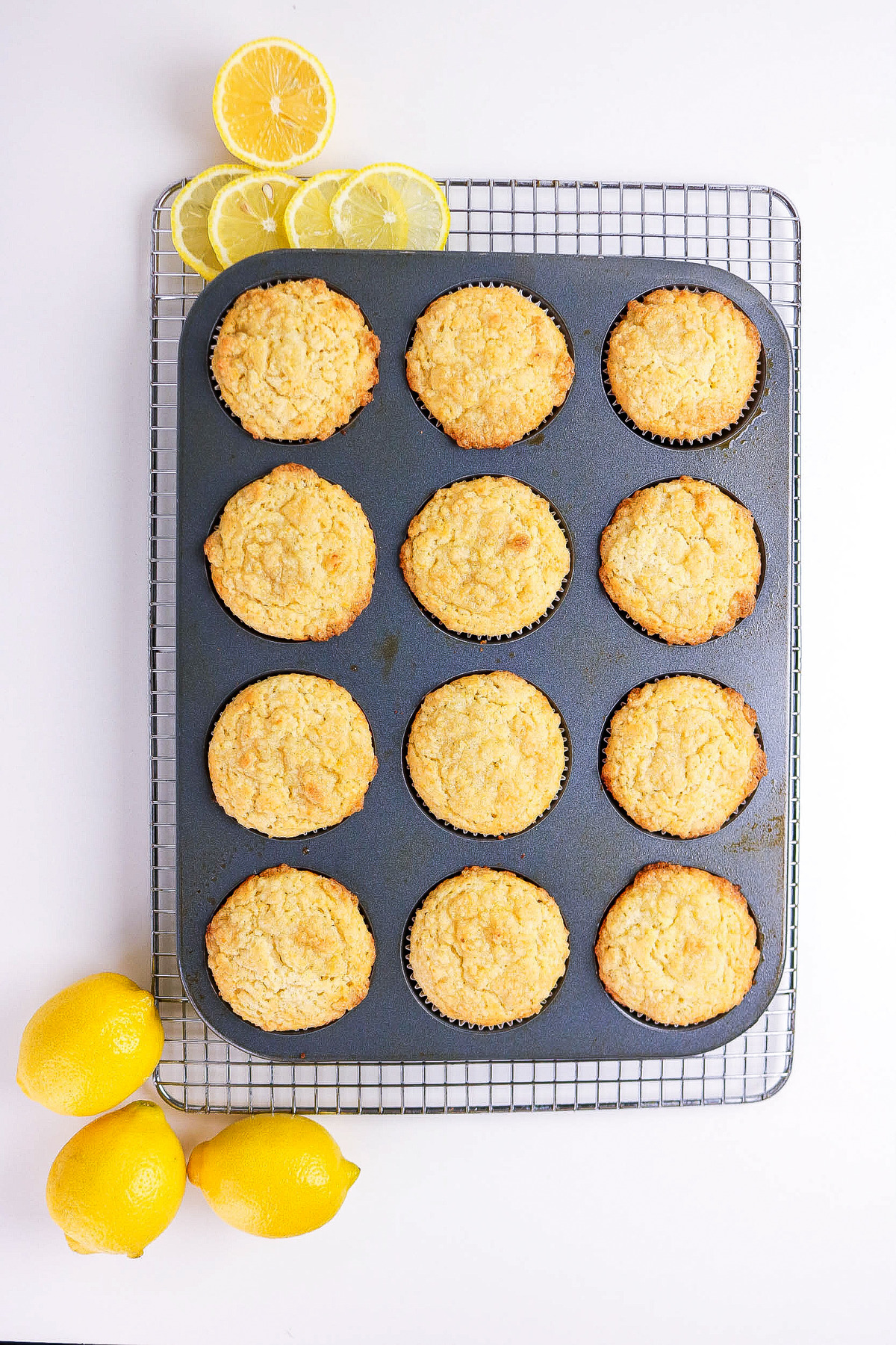 Baked lemon muffins in a tin over a cooling rack.