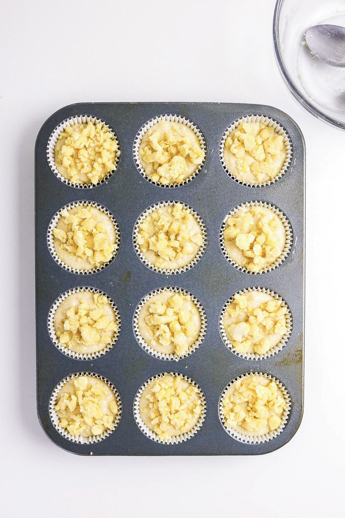 Batter divided in muffin tins topped with streusel before baking.