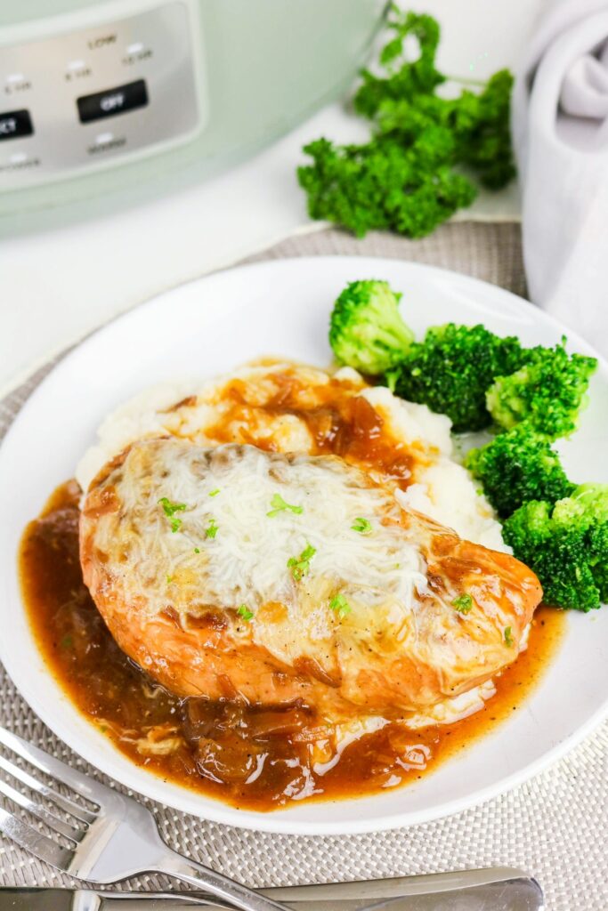 Slow cooker chicken French onion soup on a white plate with brocolli on the side.