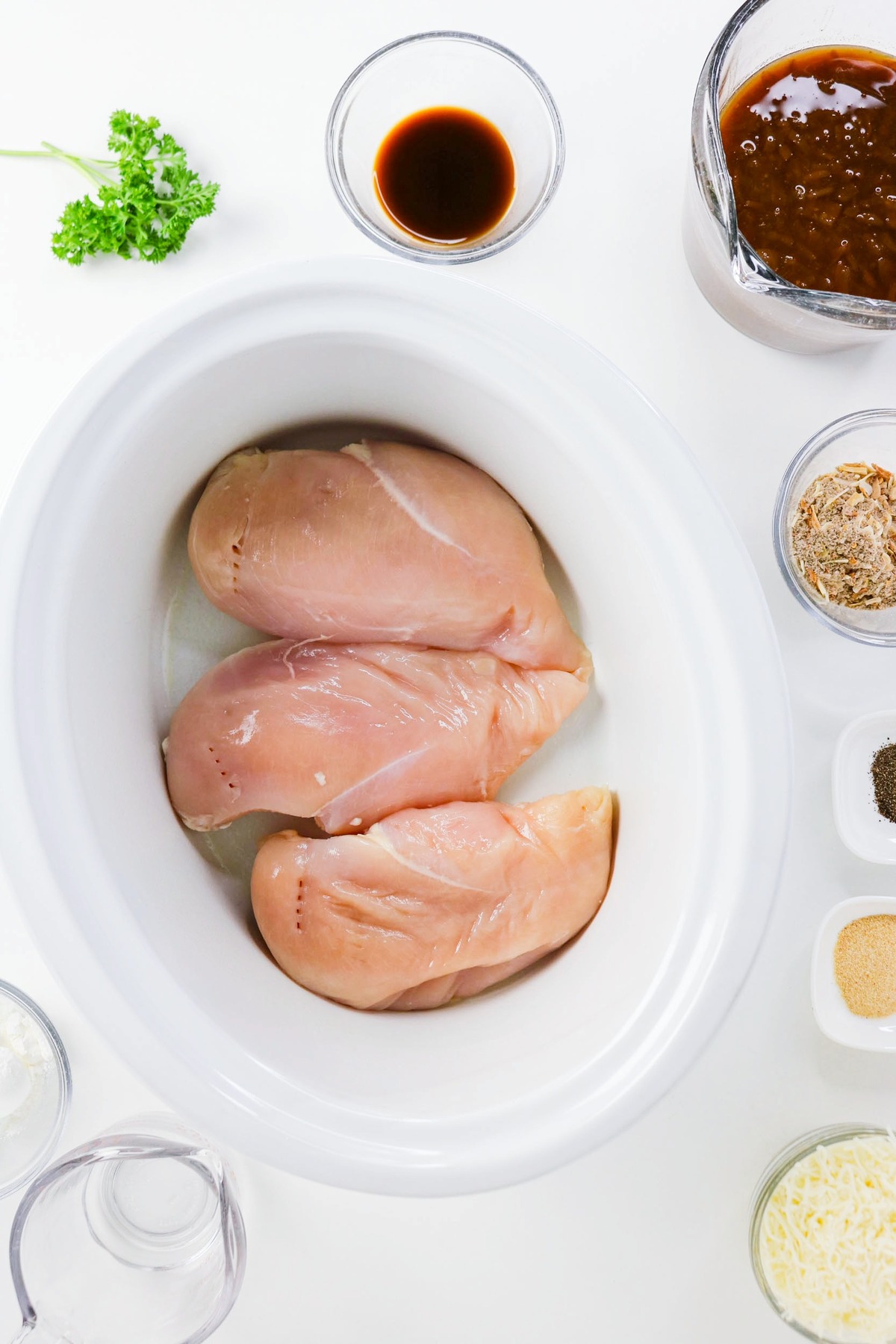 Chicken breasts placed on the bottom of a slow cooker before adding ingredients.