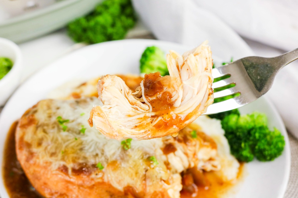A fork with a piece of chicken over a plate with broccoli on the side.