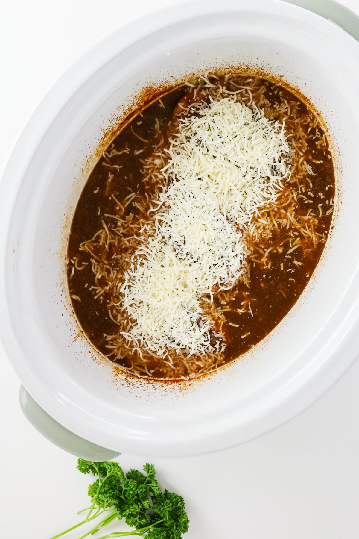 Shredded cheese over cooked chicken in a slow cooker.