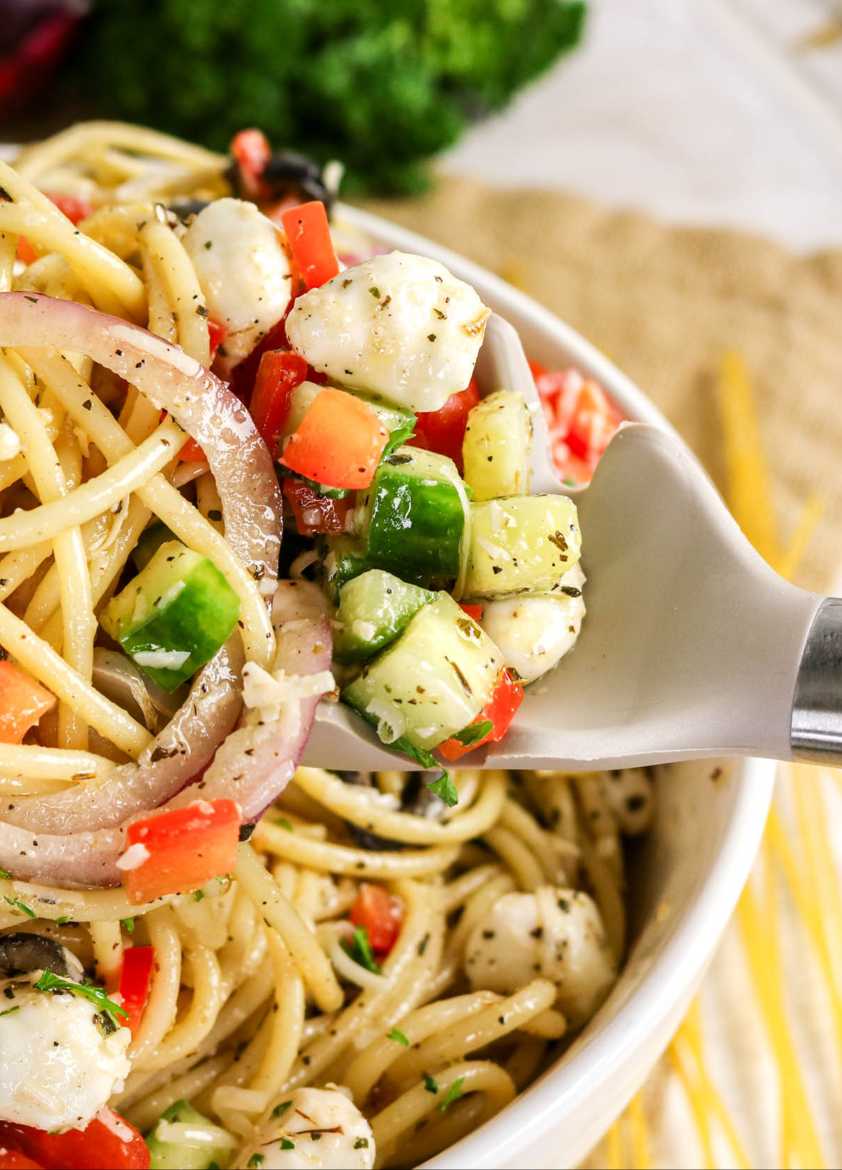 A spoonful of cold pasta with vegetables in a white serving bowl.