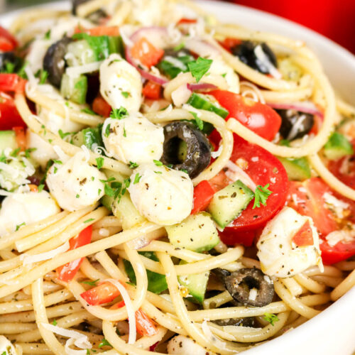 Cold pasta salad with greek inspired ingredients in a white serving bowl.