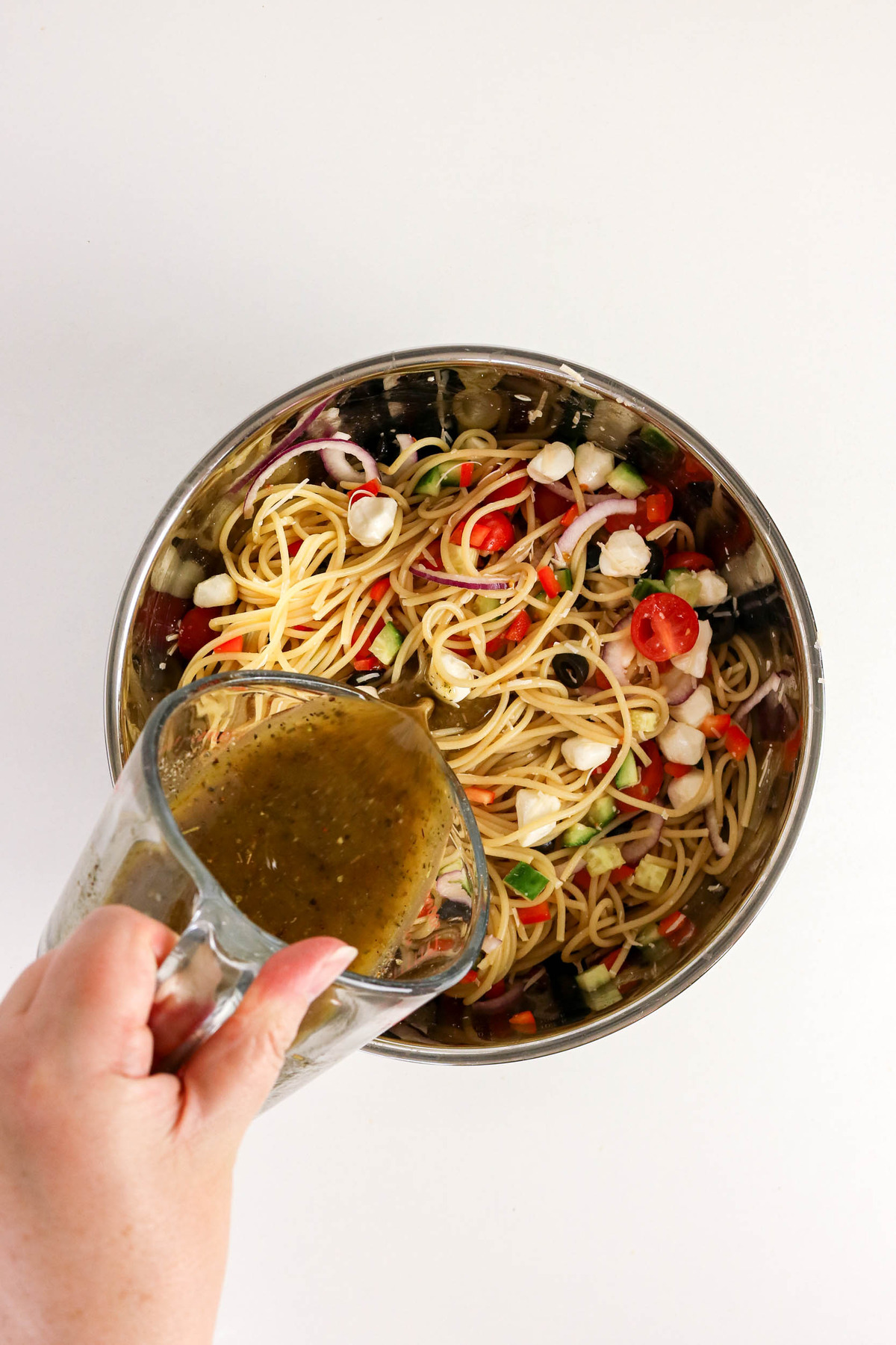 Pouring homemade Italian dressing over cold spaghetti.