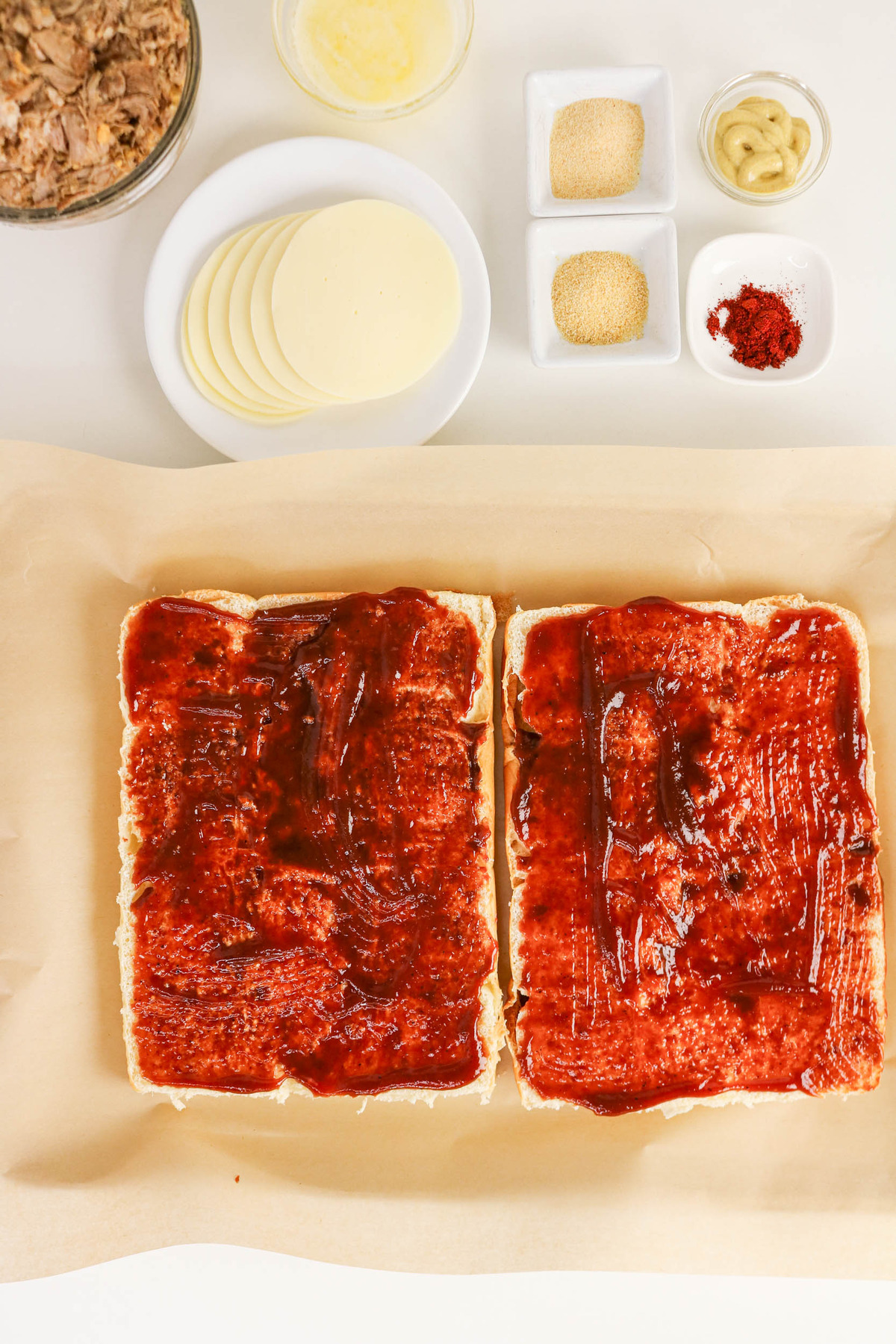 Sliced Hawaiian rolls with BBQ sauce spread on them.