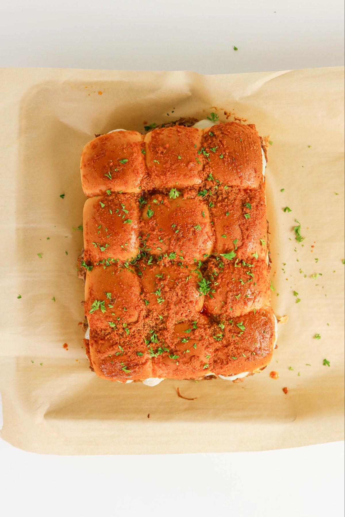 Baked BBQ pulled pork sliders on a piece of parchment paper.