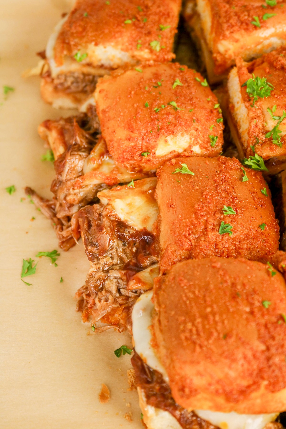 Overhead view of sliders with pulled pork and melted cheese on parchment paper.