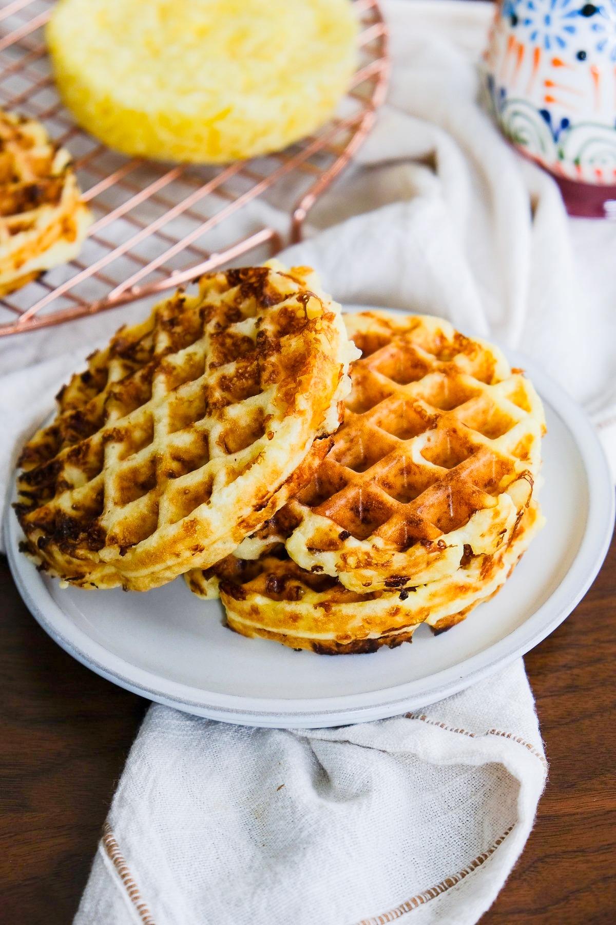 Overhead view of chaffles on a plate with chaffle on a cooling rack in the background.