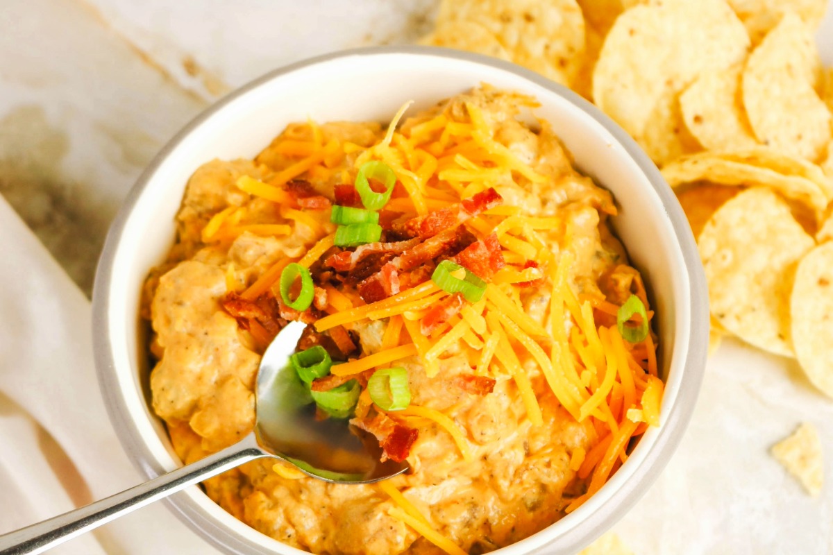 Cheesy dip in a white bowl with tortilla chips on the side.
